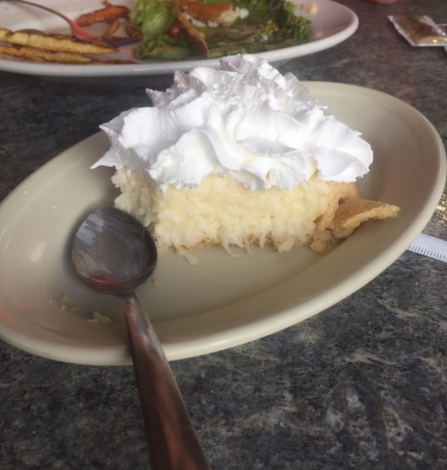 A slice of creamy dessert topped with whipped cream on a plate, with a spoon beside it.