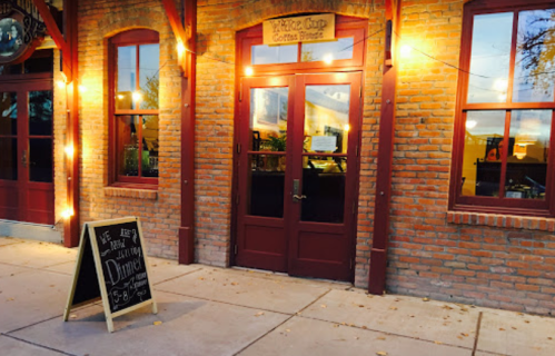 A brick building with a wooden door and a chalkboard sign outside, indicating a coffee shop and dinner service.