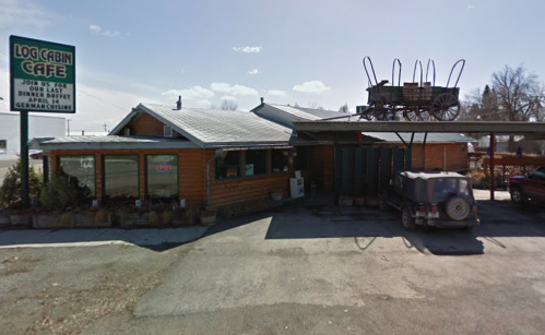 A rustic log cabin-style restaurant with a wagon on the roof, featuring a sign for German cuisine and an open sign.