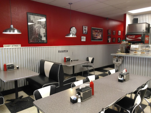Retro diner interior with red walls, black and white seating, checkered floor, and vintage decor.