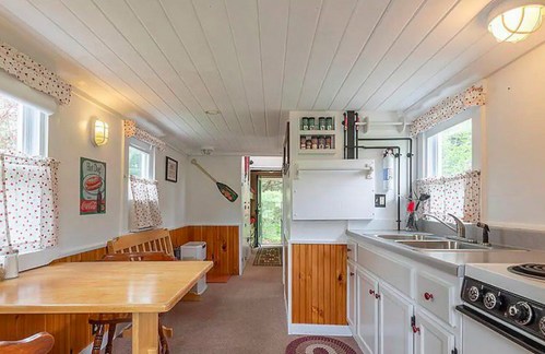 Cozy kitchen with wooden table, white cabinets, and large windows, featuring a rustic decor and a view of the outdoors.