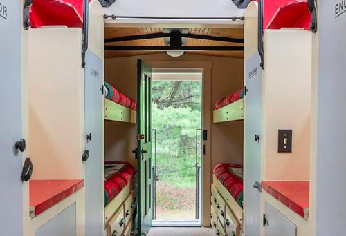 Interior view of a cozy cabin with two sets of bunk beds and a door leading to a forested area outside.
