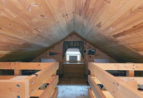Cozy attic room with wooden walls, two beds, and a window air conditioner.