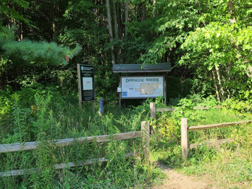 Signage at the entrance of Dowagiac Woods, surrounded by lush greenery and a wooden fence.