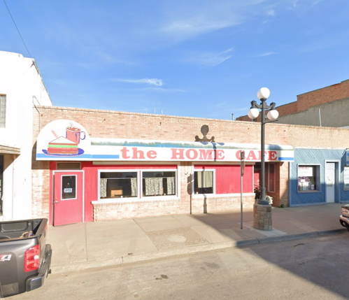 Exterior of the Home Cafe, featuring a colorful sign, large windows, and a classic brick facade on a sunny day.