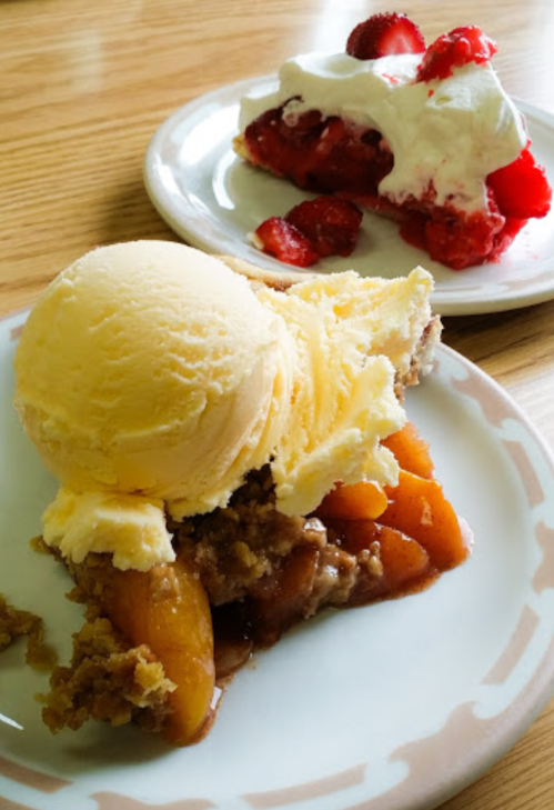 A slice of peach cobbler topped with vanilla ice cream, alongside a slice of strawberry pie with whipped cream.