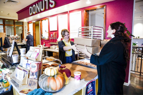 A customer receives two boxes of donuts from a smiling employee at a vibrant donut shop counter.
