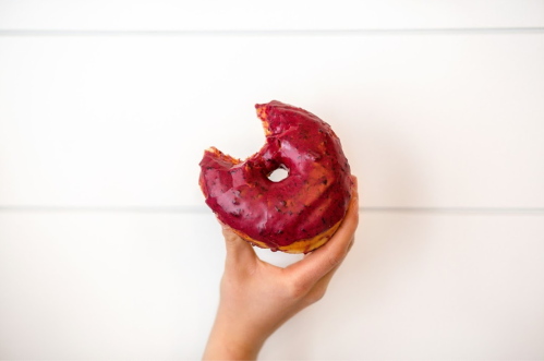 A hand holding a partially eaten donut with a vibrant red glaze against a white background.