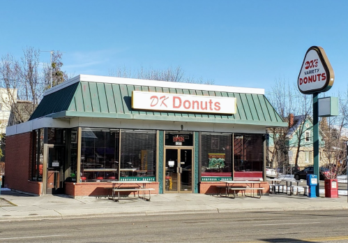 A storefront of DK Donuts with a green roof, large windows, and a sign indicating it's open. Outdoor seating is visible.