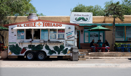 A colorful food truck named "El Chile Toreado" with outdoor seating and patrons enjoying their meals.