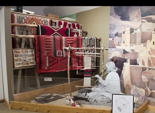 A display featuring traditional textiles, a weaving setup, and a figure crafting in a museum setting.