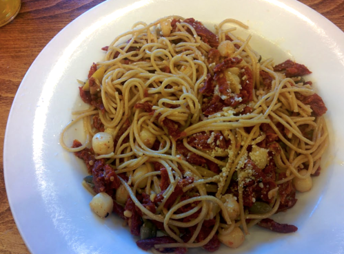 A plate of spaghetti with sun-dried tomatoes, scallops, and a sprinkle of cheese on top.