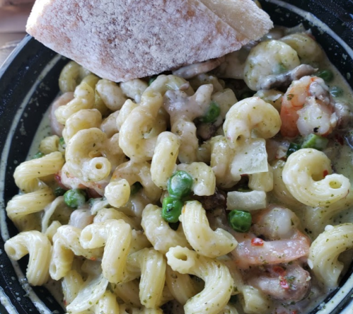 A bowl of creamy pasta with vegetables and shrimp, served with a piece of bread on the side.
