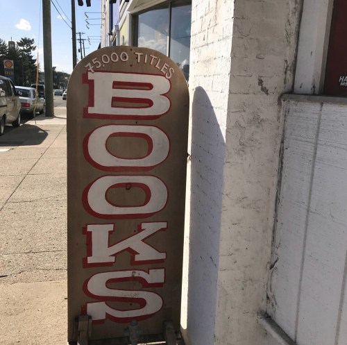 A weathered sign on the sidewalk reads "BOOKS" with "75,000 TITLES" below it, indicating a bookstore.