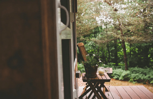 A wooden chair and small table with a potted plant on a porch, surrounded by lush greenery.