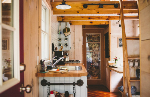 Cozy kitchen in a wooden cabin, featuring a sink, stove, and rustic decor with natural light streaming in.