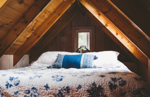 Cozy attic bedroom with a wooden ceiling, a floral quilt, and a blue decorative pillow on a bed.