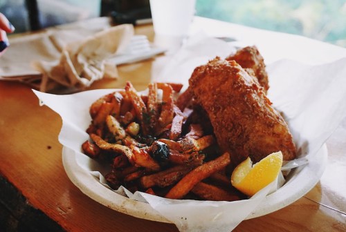 A plate of crispy fried fish with seasoned fries and a lemon wedge, served on a wooden table.