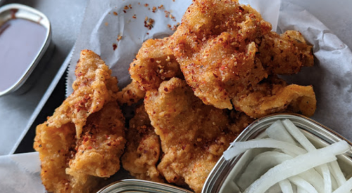 Crispy fried chicken pieces sprinkled with spices, served with sliced onions on the side.
