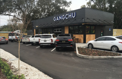 A modern restaurant named "Gangchu" with several parked cars in front and trees nearby.