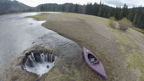 A purple kayak rests near a small waterfall flowing into a circular hole in a dry, grassy landscape.