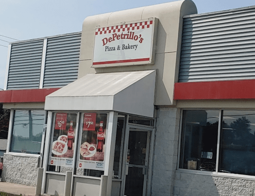 Exterior of DePetrillo's Pizza & Bakery, featuring a red and white sign and large windows displaying menu items.