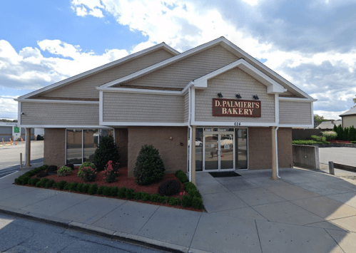 Exterior of D. Palmieri's Bakery, featuring a light brown building with a sign, landscaped area, and cloudy sky.