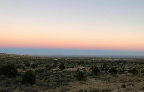 A serene landscape at dusk, featuring rolling hills and a gradient sky transitioning from blue to soft pink.