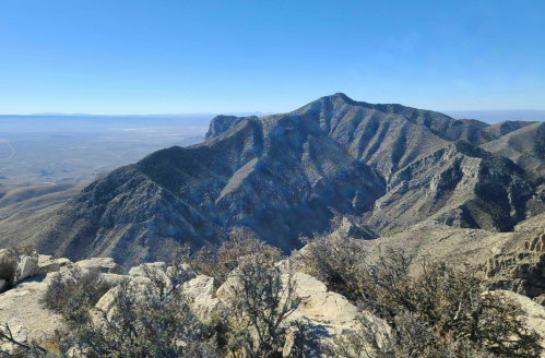A panoramic view of rugged mountains under a clear blue sky, with valleys stretching into the distance.
