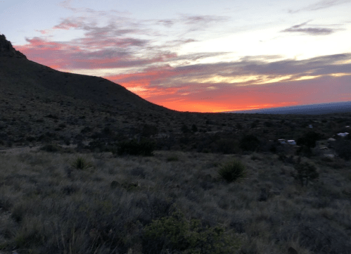 A vibrant sunset over a mountainous landscape, with colorful clouds and a silhouette of hills in the foreground.