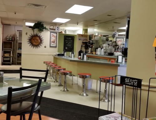 A cozy diner interior featuring a counter with stools, a sun decoration, and tables in a casual setting.