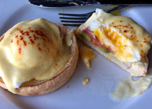A plate with a half-eaten eggs Benedict on an English muffin, topped with hollandaise sauce and paprika.