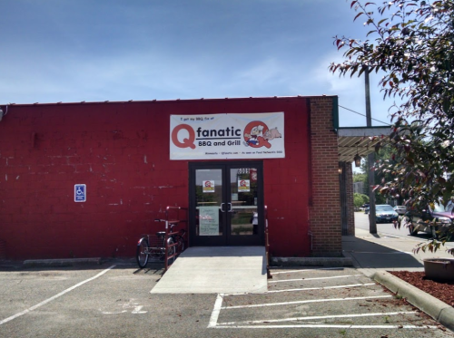 Exterior of Qfanatic BBQ and Grill, featuring a red brick wall and a sign above the entrance. Accessible parking visible.