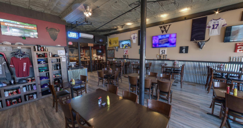 A spacious restaurant interior with wooden tables, chairs, and sports memorabilia on the walls, featuring multiple TVs.