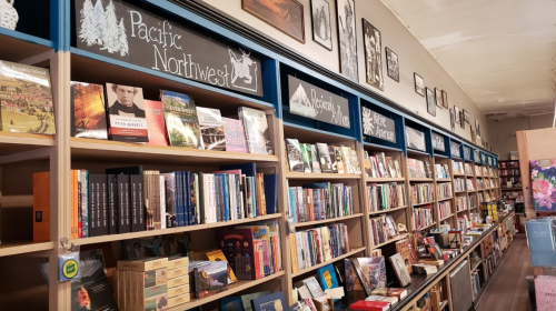 A cozy bookstore with shelves filled with books, labeled "Pacific Northwest" and "Pacific History."