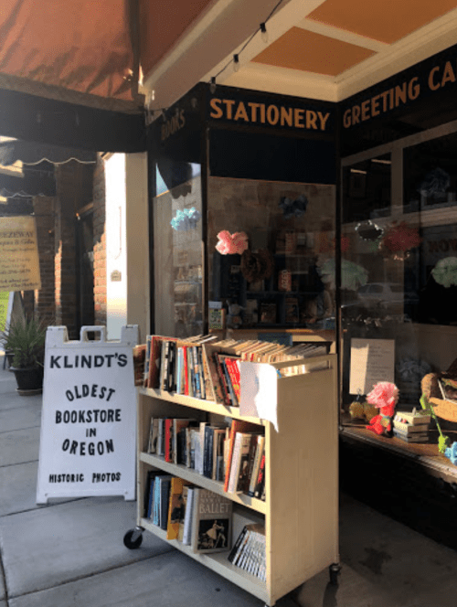 A quaint bookstore entrance with a sign reading "Klindt's Oldest Bookstore in Oregon" and a display of books outside.