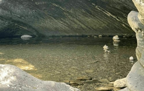 A serene water scene with smooth stones stacked in a shallow pool beneath a rocky overhang.