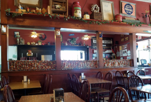 Cozy restaurant interior with wooden tables, decorative wall art, and a counter adorned with colorful items.