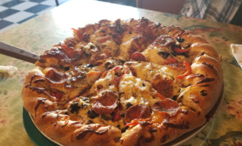 A freshly baked pizza with pepperoni, bell peppers, and a stuffed crust, served on a green table.