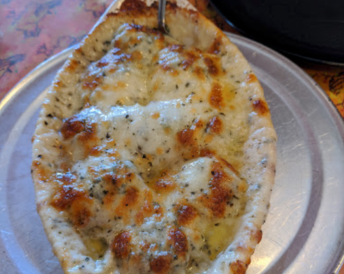 A cheesy, baked dish served in a boat-shaped bread, with a golden, bubbly topping.