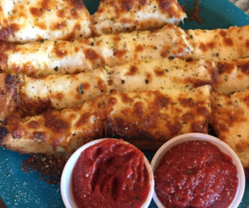 Cheesy garlic breadsticks on a blue plate, served with two small cups of marinara sauce.
