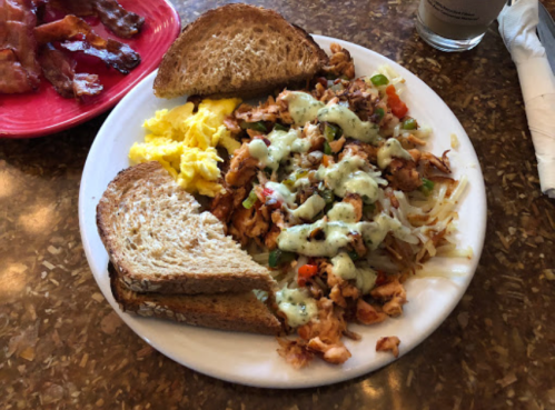 A plate of scrambled eggs, seasoned chicken, hash browns, and two slices of whole grain toast.