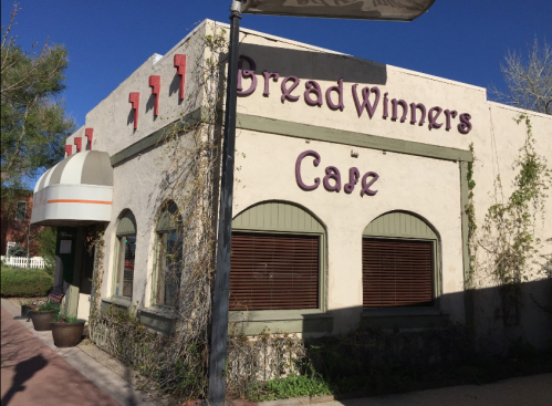 Exterior of Bread Winners Cafe, featuring a stucco facade, arched windows, and a striped awning under a clear blue sky.