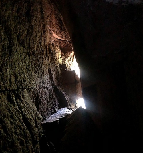 A narrow crevice in a rocky cave, with light streaming through from the outside.
