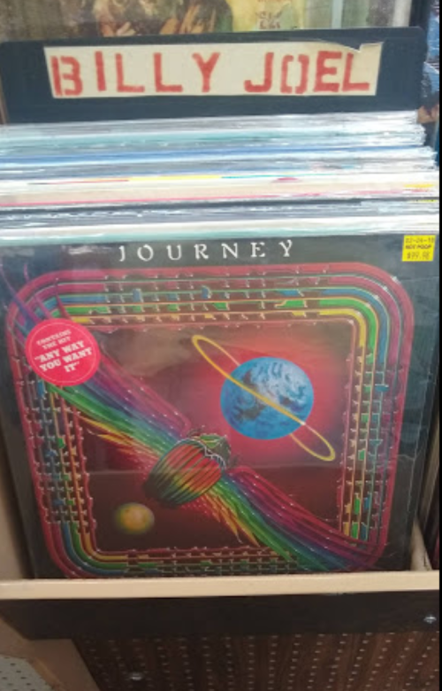 A display of vinyl records featuring "Journey" and "Billy Joel" album covers in a record store.