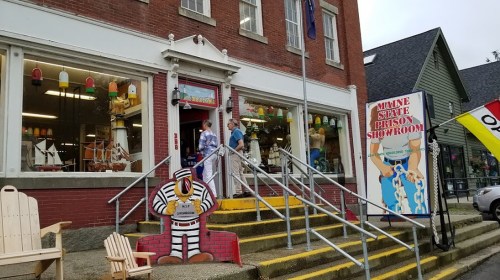 A colorful storefront with steps leading up, featuring a sign for a museum and decorative items in the windows.
