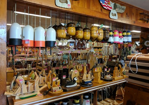 A display of colorful buoys and wooden sailboat models in a shop with wooden walls and various nautical decorations.