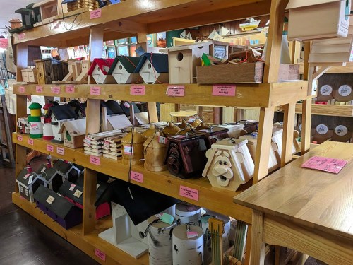 A wooden shelf displaying various colorful birdhouses and craft items in a shop.