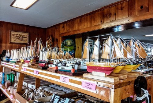A display of colorful model ships on wooden shelves in a rustic shop, showcasing various sailing designs.