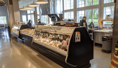 A modern deli counter displaying various meats and cheeses, with staff members working in a bright, spacious setting.